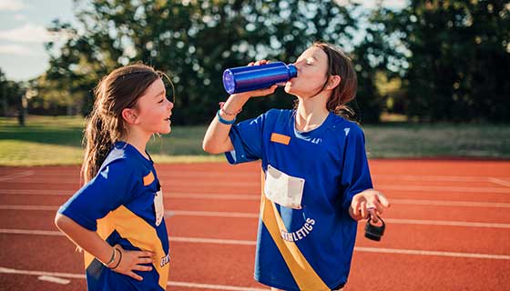 Two girls on a track field drinking water after training