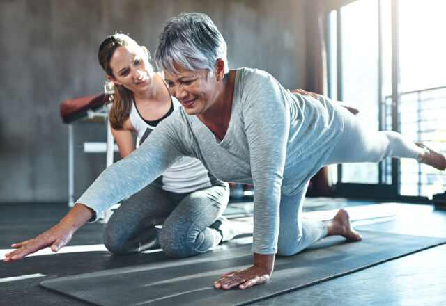 Physical therapist working with older woman on a yoga mat.
